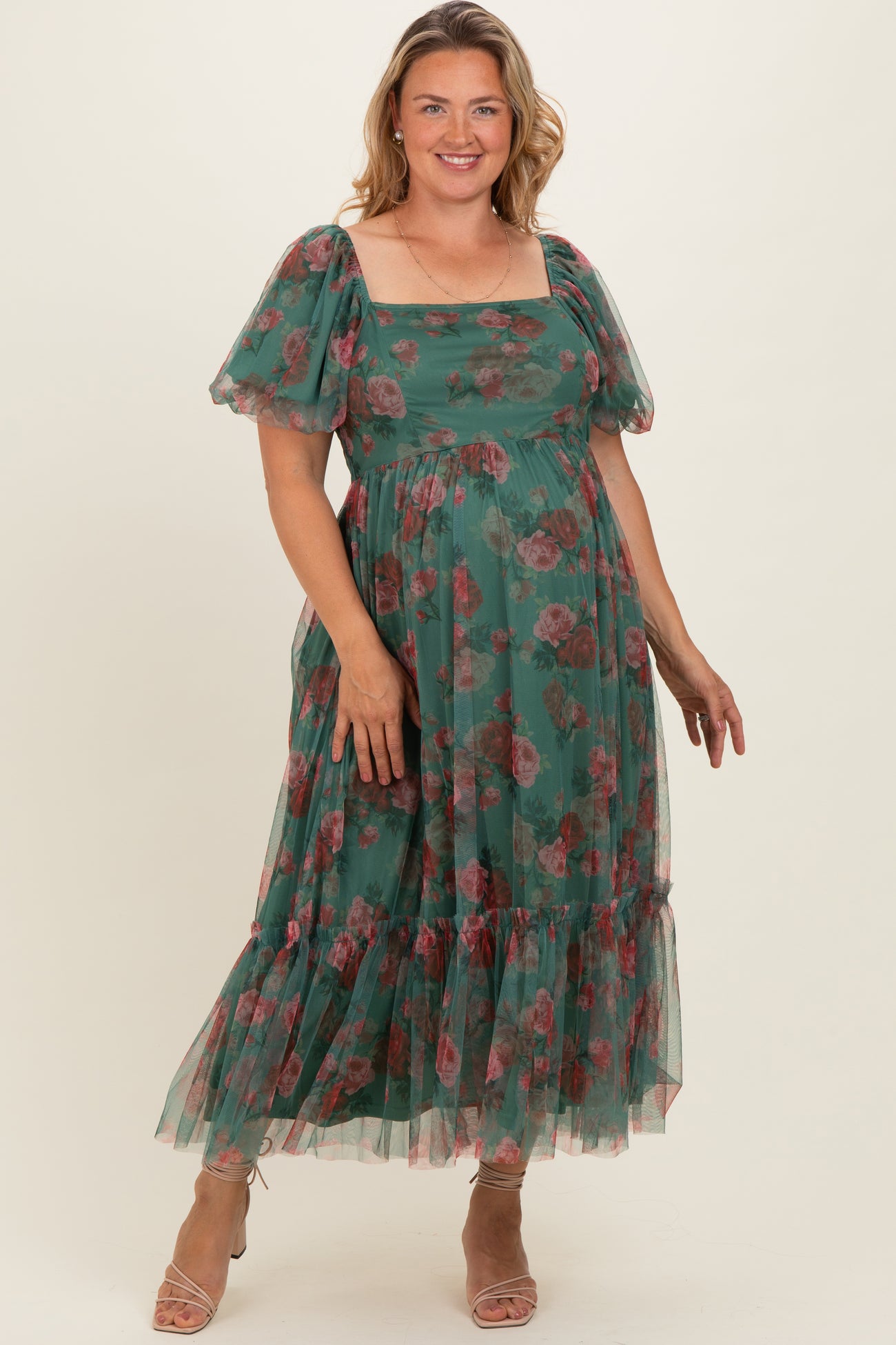 woman wearing a green floral maternity plus dress with puff sleeves and a tiered skirt, showing her baby bump