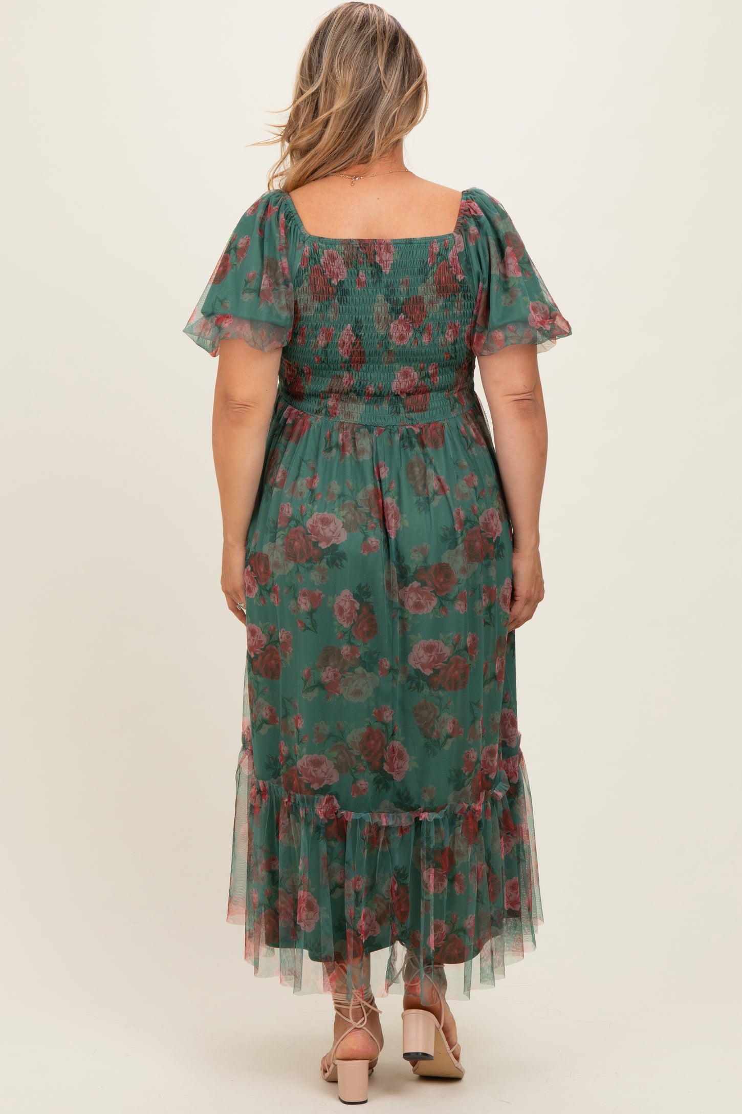 woman wearing a green floral maternity plus dress with a smocked bodice and ruffled hem, seen from the back