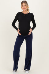 woman wearing a black long sleeve maternity top and navy wide leg maternity pants, holding her baby bump