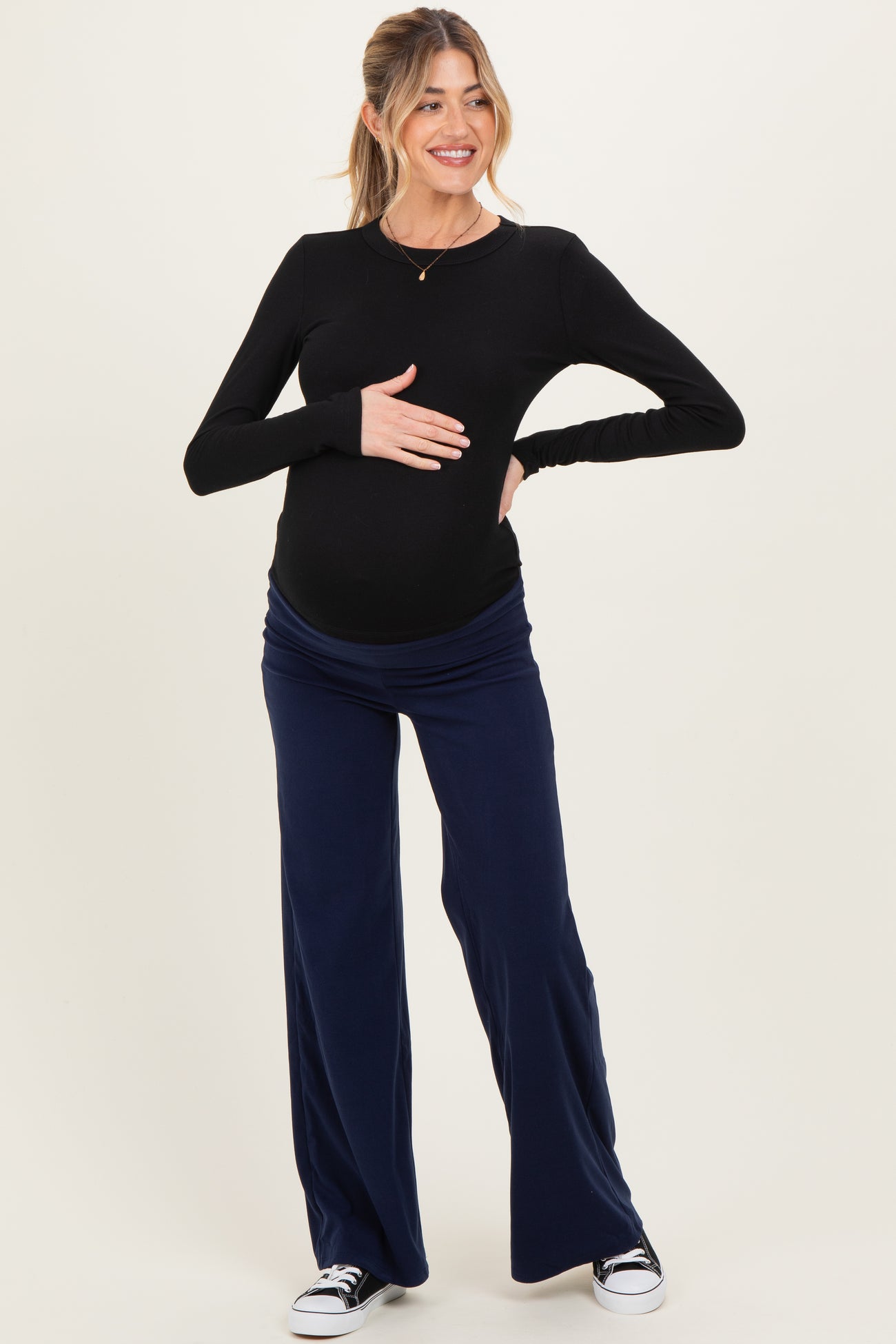 woman wearing a black long sleeve maternity top and navy wide leg maternity pants, showcasing her baby bump