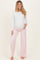 woman wearing a white long sleeve maternity top and pink wide-leg maternity pants, showing her baby bump
