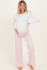 woman wearing a white long sleeve maternity top and pink maternity pants, holding her baby bump