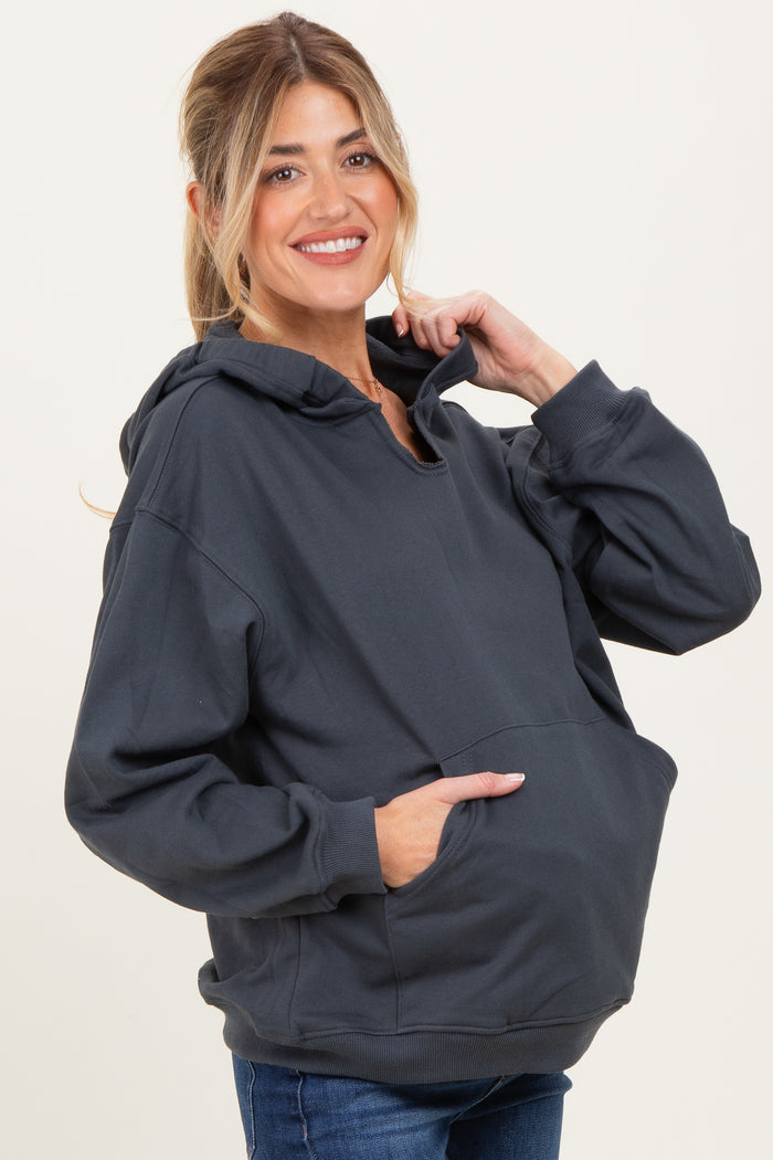 woman wearing a dark gray maternity hoodie with a front pocket and a relaxed fit, holding the hood while smiling