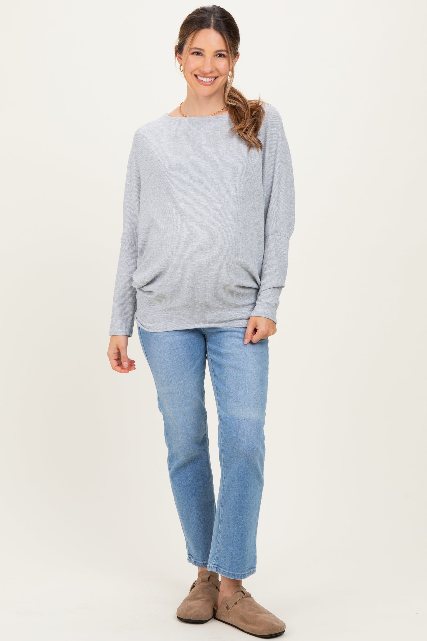 woman wearing a gray maternity sweater and blue jeans, highlighting her baby bump