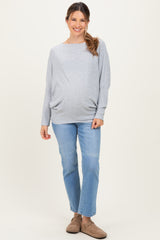 woman wearing a gray maternity sweater and blue jeans, highlighting her baby bump