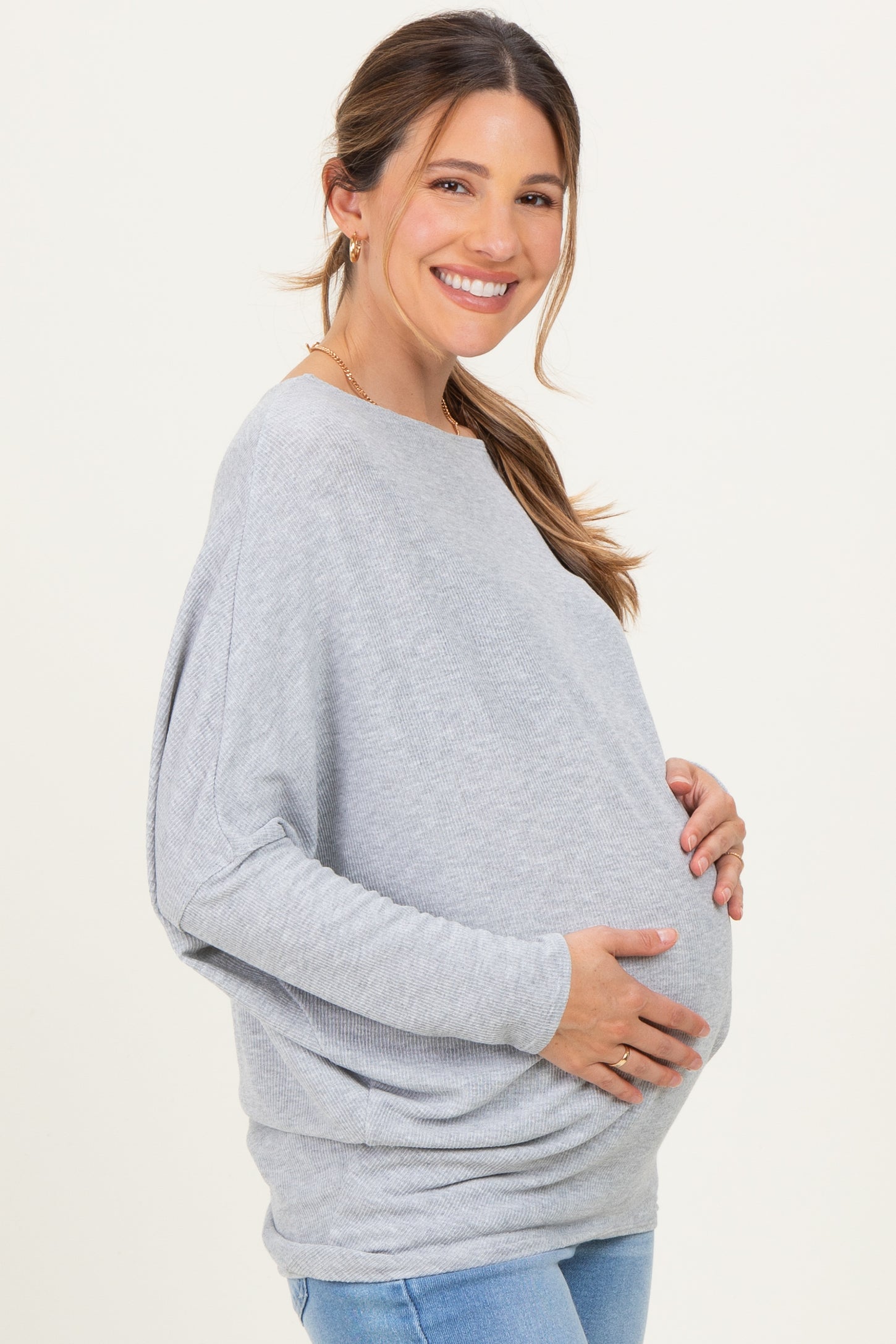 woman wearing a gray oversized maternity sweater and holding her baby bump
