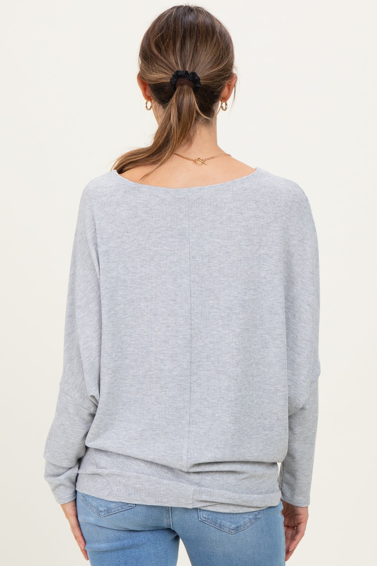 woman wearing a light gray maternity sweater with a loose fit and drop sleeves, viewed from the back