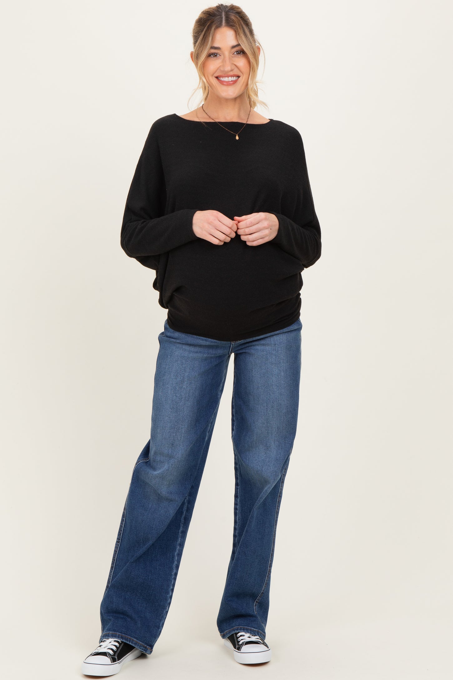 woman wearing a black oversized maternity sweater and blue flared jeans, showing her baby bump