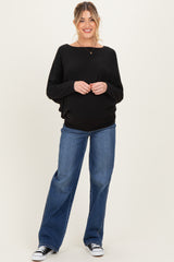 woman wearing a black oversized maternity sweater and blue flared jeans, showing her baby bump