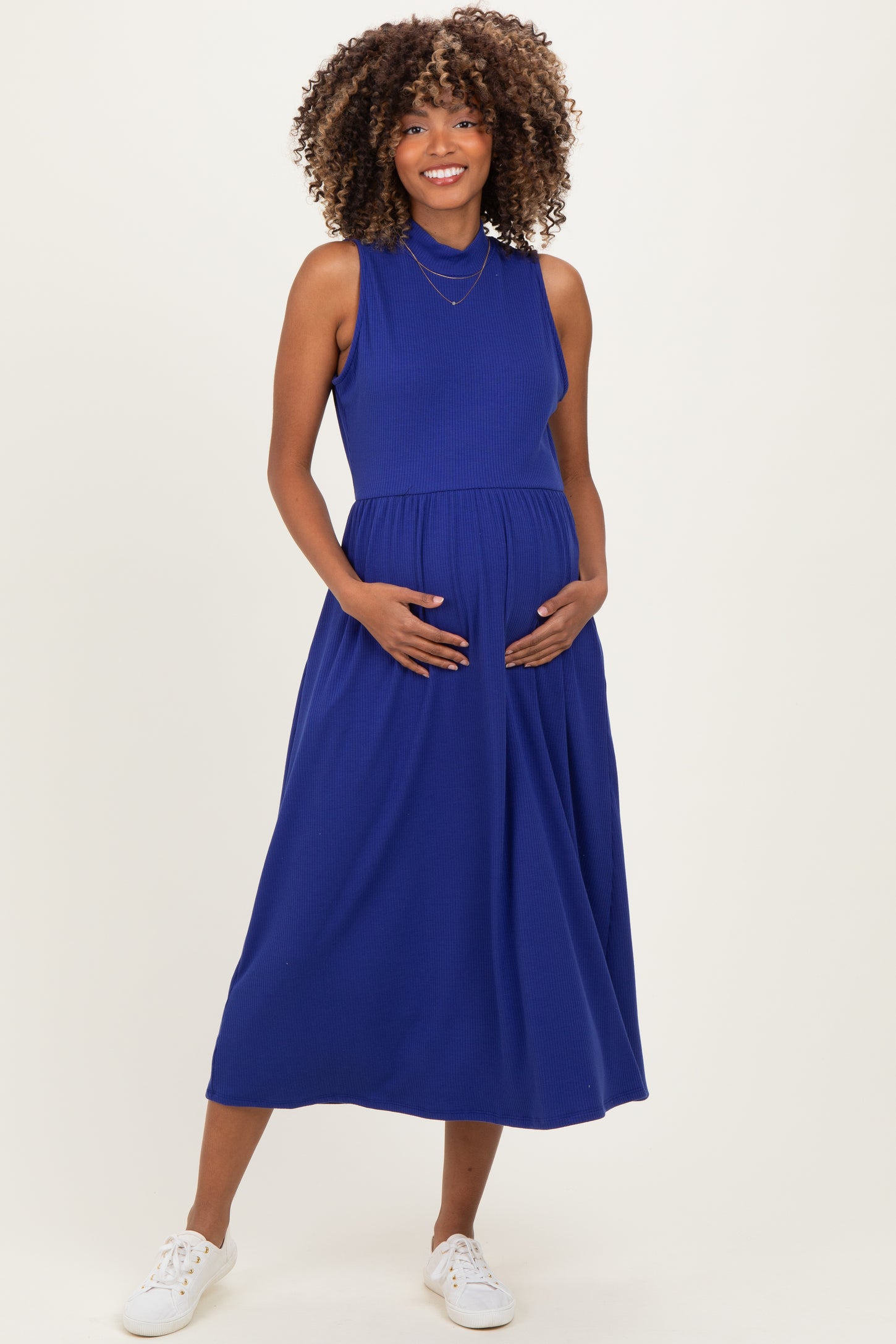 woman wearing a bright blue sleeveless maternity dress with a fitted bodice and a flowing skirt, holding her baby bump