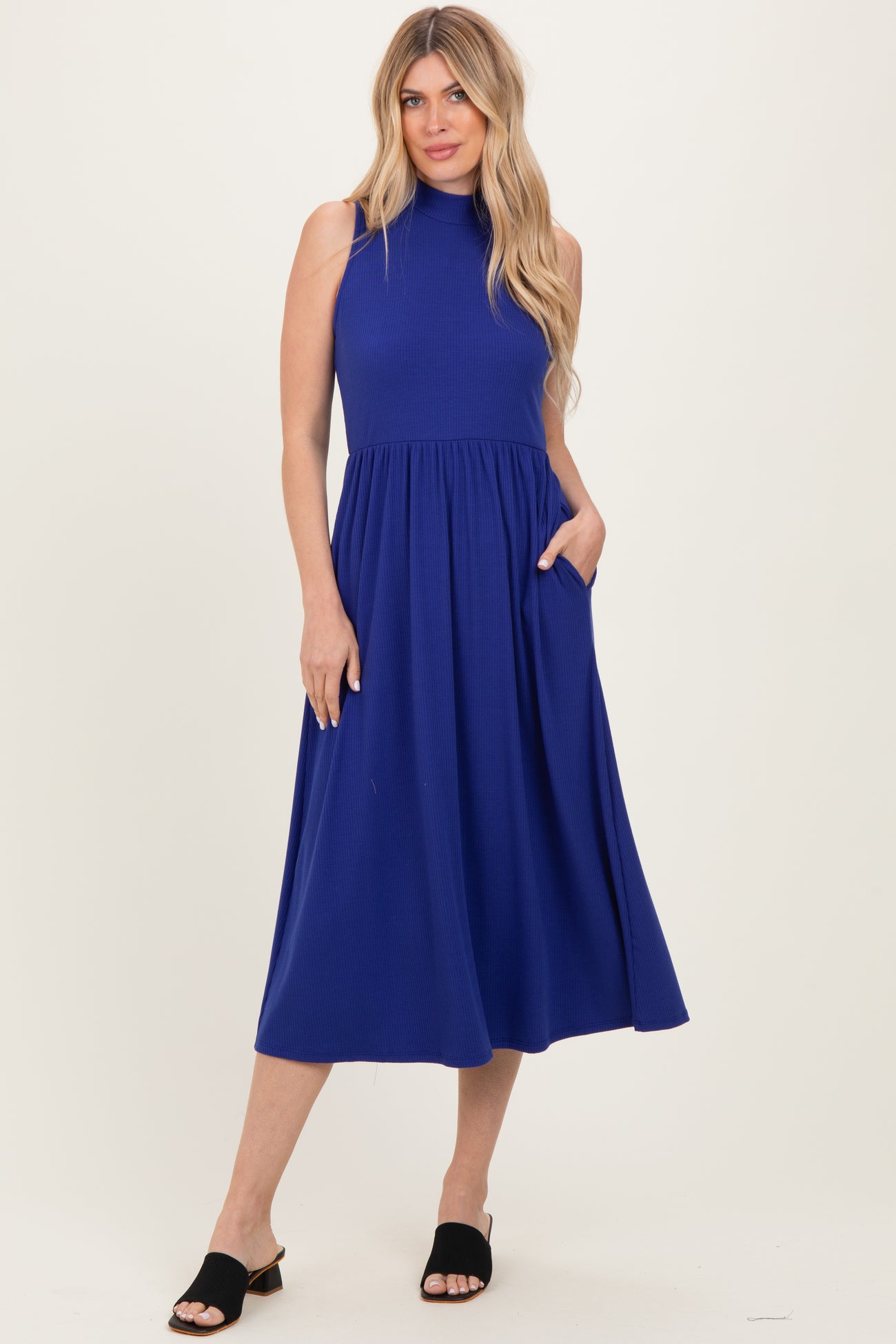 woman wearing a sleeveless royal blue midi dress with a high neck and pockets, standing in a relaxed pose