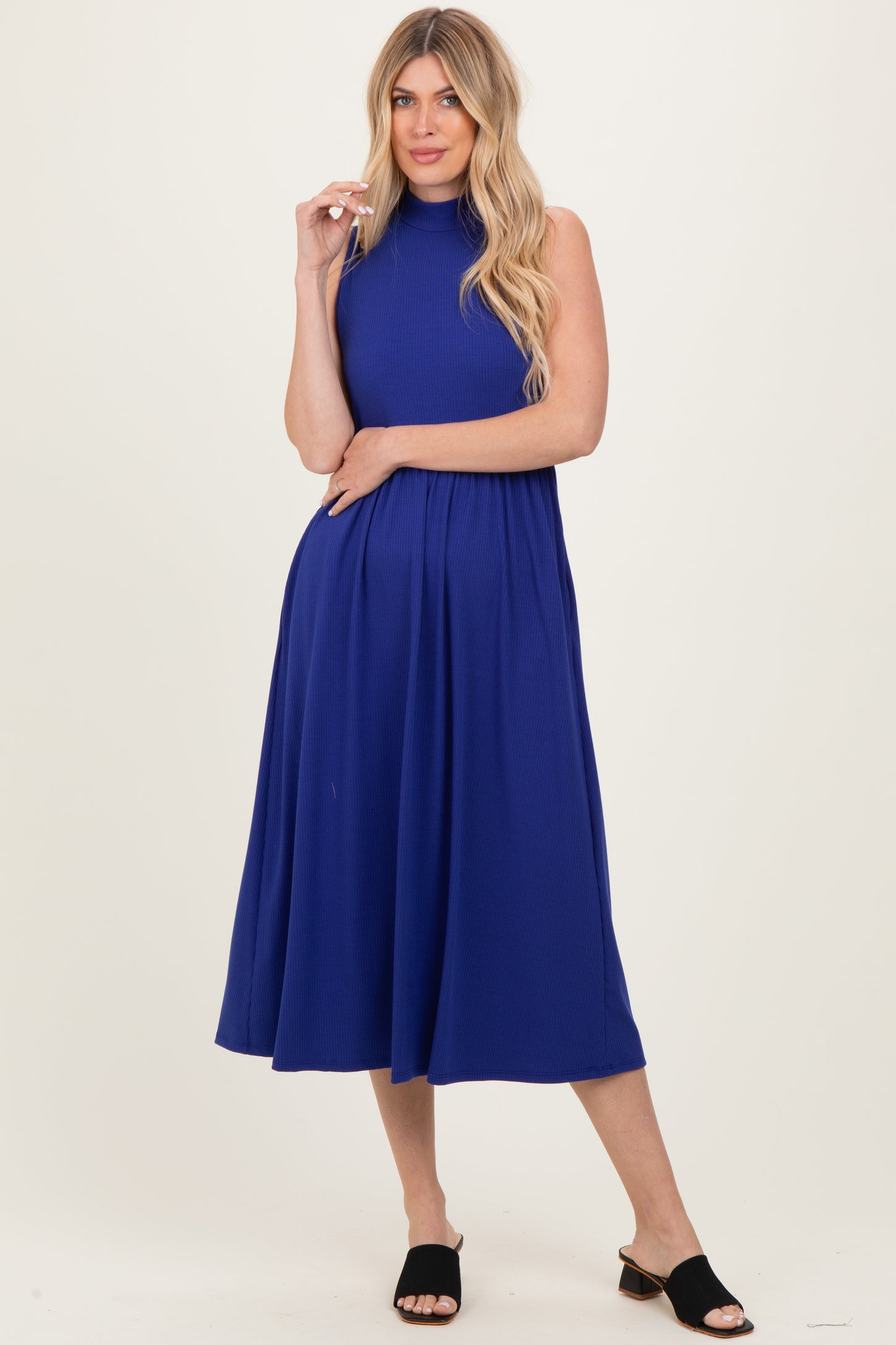 woman wearing a sleeveless royal blue midi dress with a high neckline and flared skirt, standing in a relaxed pose
