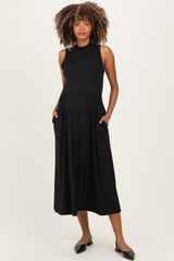 woman wearing a black ribbed maternity dress with a high neckline and pockets, showing her baby bump