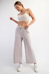 woman wearing a beige cropped tank top and light gray wide-leg pants, standing in a casual pose with white sneakers