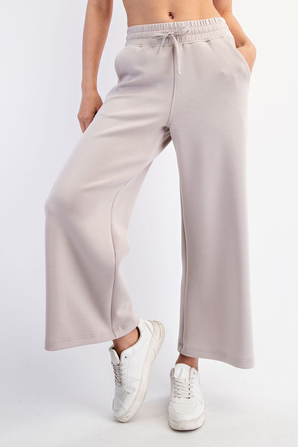 woman wearing light gray wide-leg sweatpants with an elastic waistband and side pockets, paired with white sneakers