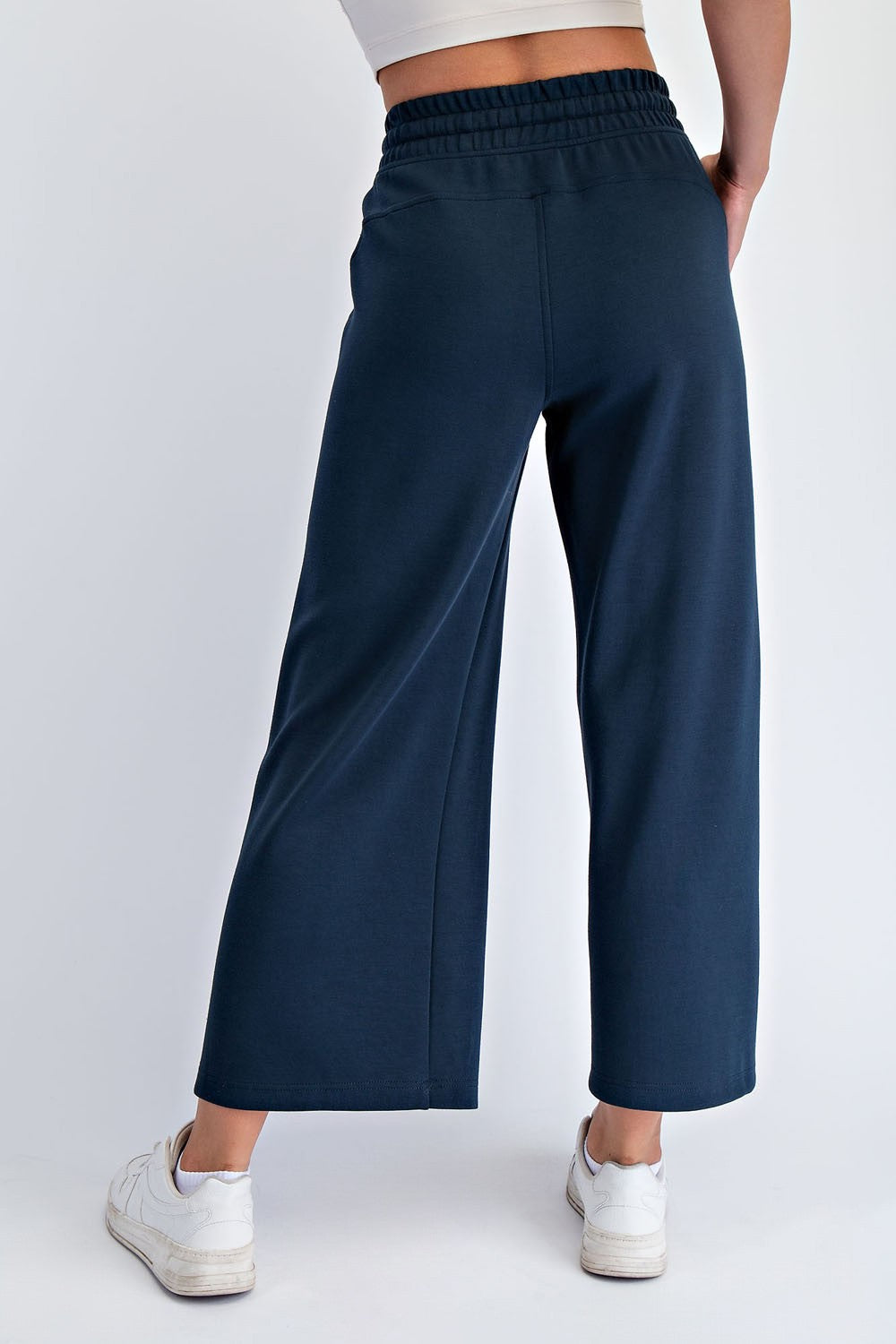 woman wearing dark navy wide-leg sweatpants, viewed from the back with a white cropped top and sneakers