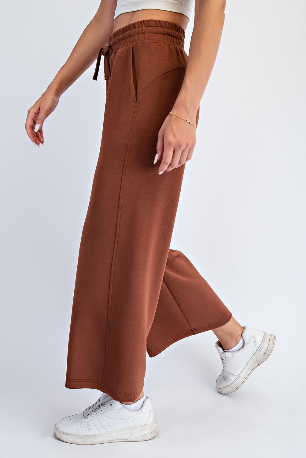 woman wearing brown wide-leg lounge pants with a drawstring waist, paired with white sneakers