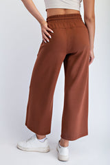 woman wearing rust colored wide-leg pants with an elastic waistband and white sneakers, viewed from the back