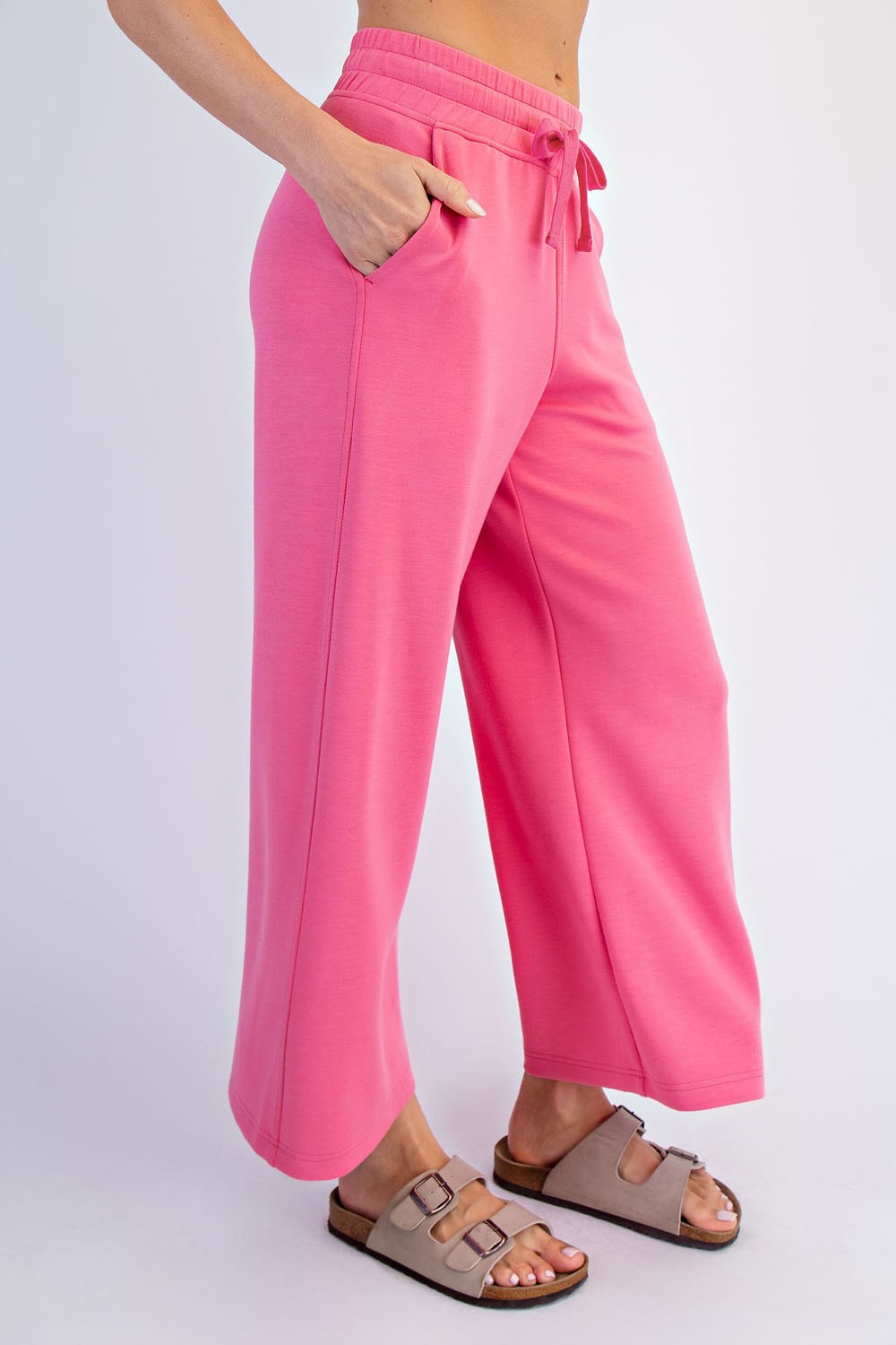 woman wearing bright pink wide-leg sweatpants with pockets and a drawstring waist, paired with tan sandals