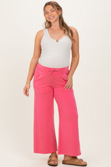 woman wearing a white ribbed tank top and pink maternity wide leg pants, showing her baby bump