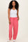 woman wearing a white tank top and pink relaxed fit pants with pockets, standing and smiling