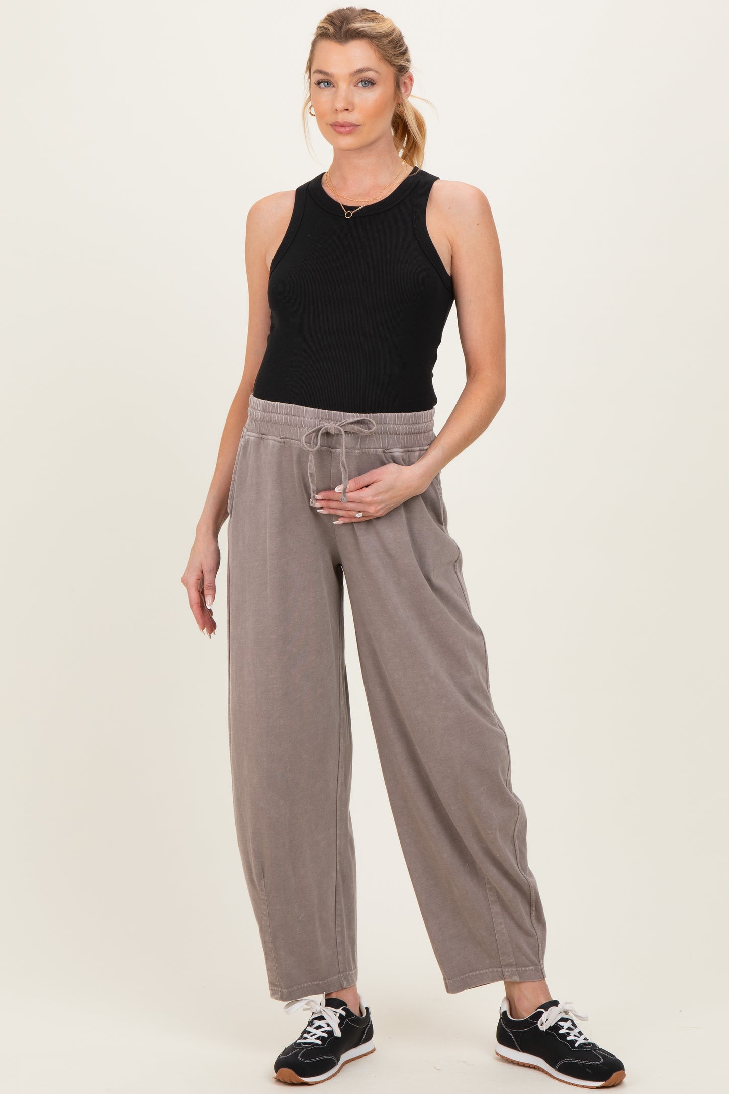 woman wearing a black ribbed maternity tank top and light gray wide-leg maternity pants, holding her baby bump