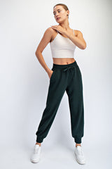 woman wearing a cream cropped tank top and dark green jogger pants with elastic waistband and cuffs