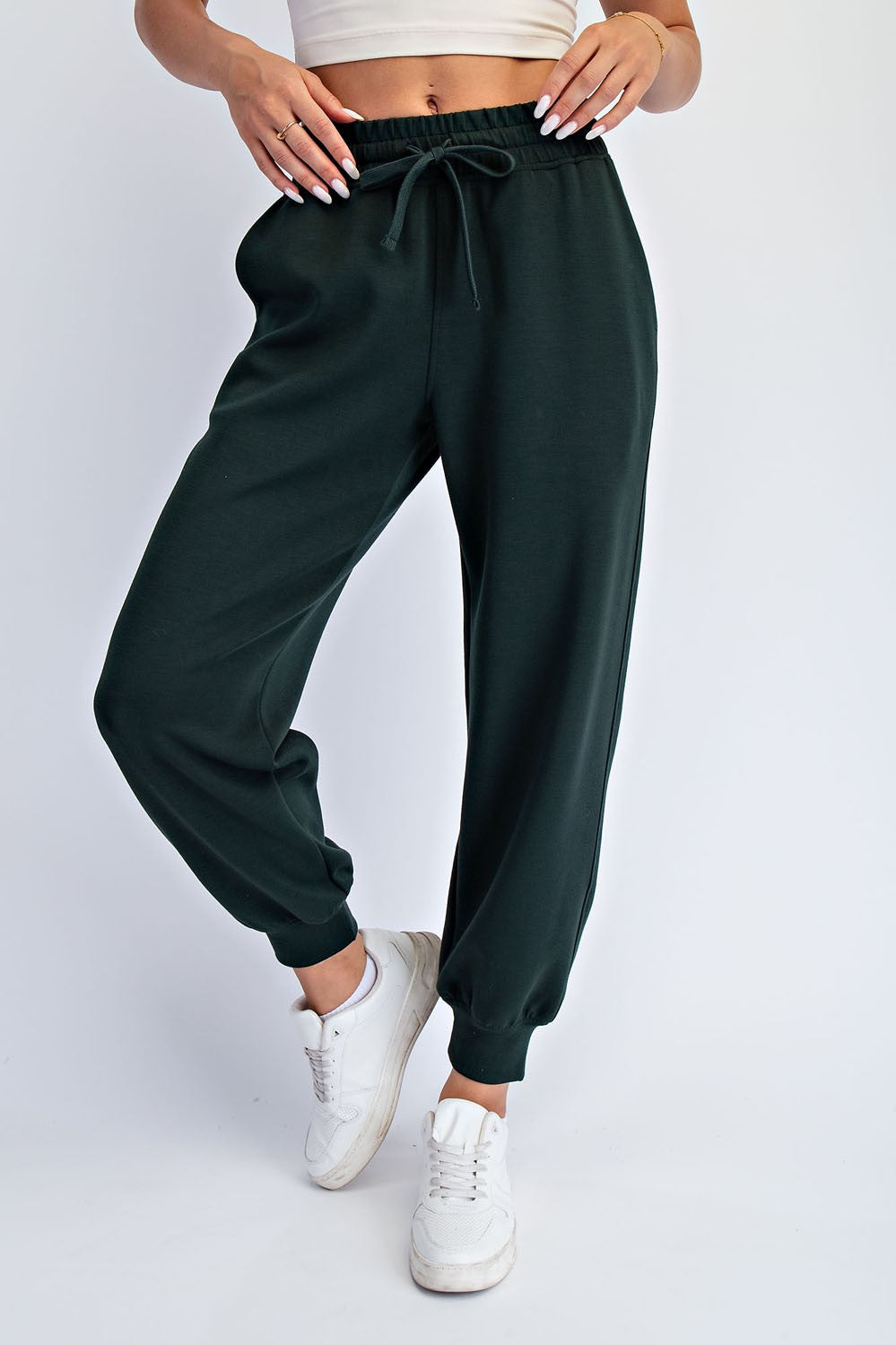 woman wearing dark green jogger pants with an elastic waistband and cuffed ankles, paired with a cropped top