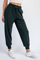 woman wearing dark green jogger pants and white sneakers, standing with one leg slightly forward