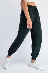 woman wearing dark green relaxed fit sweatpants with elastic ankle cuffs and side pockets, paired with white sneakers