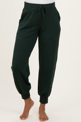 woman wearing dark green maternity jogger pants with an elastic waistband and pockets, standing barefoot