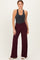 woman wearing a dark gray sleeveless top and burgundy wide-leg pants, standing with hands on hips against a light background