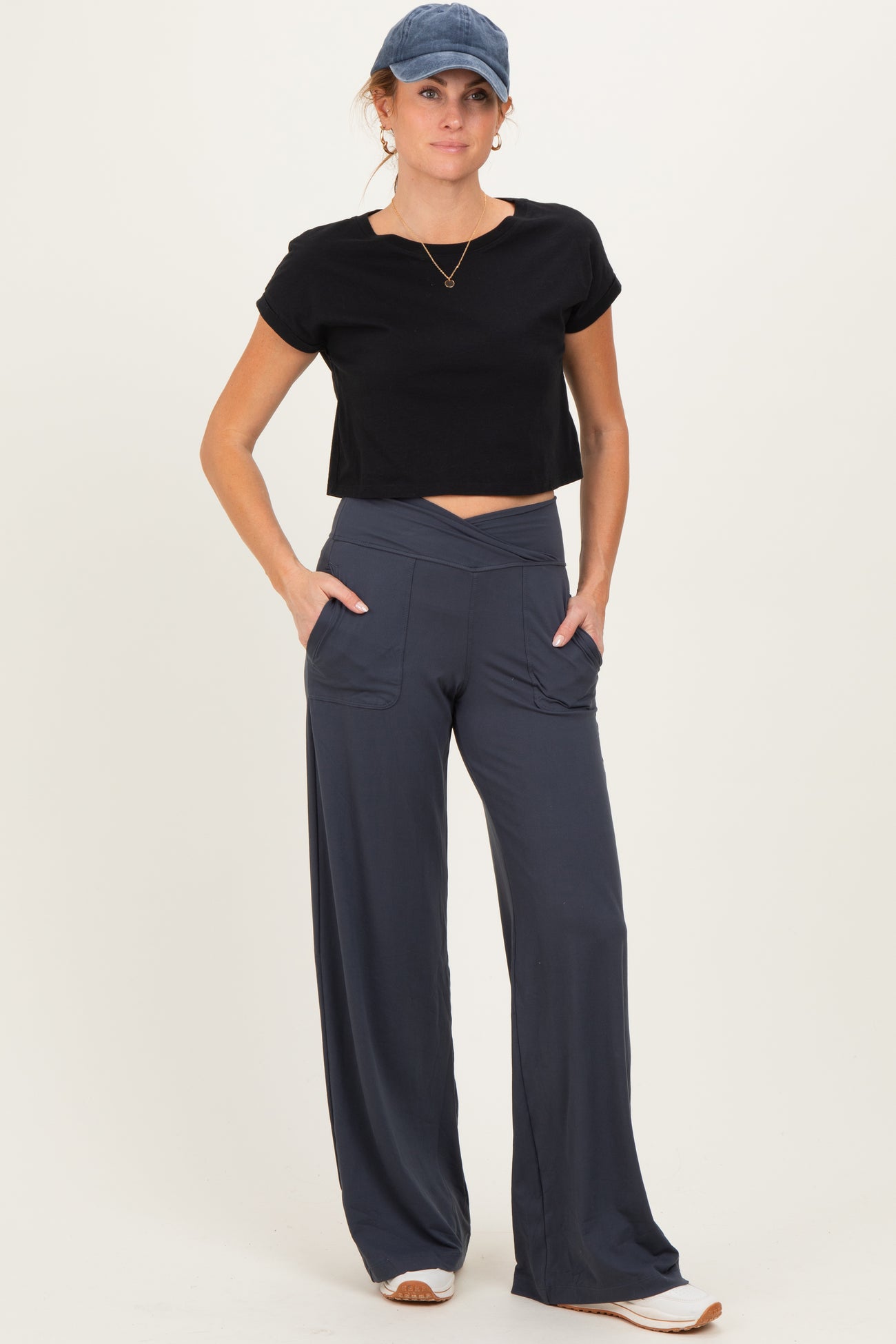 woman wearing a black cropped t-shirt and navy wide-leg pants with pockets, styled casually with a cap