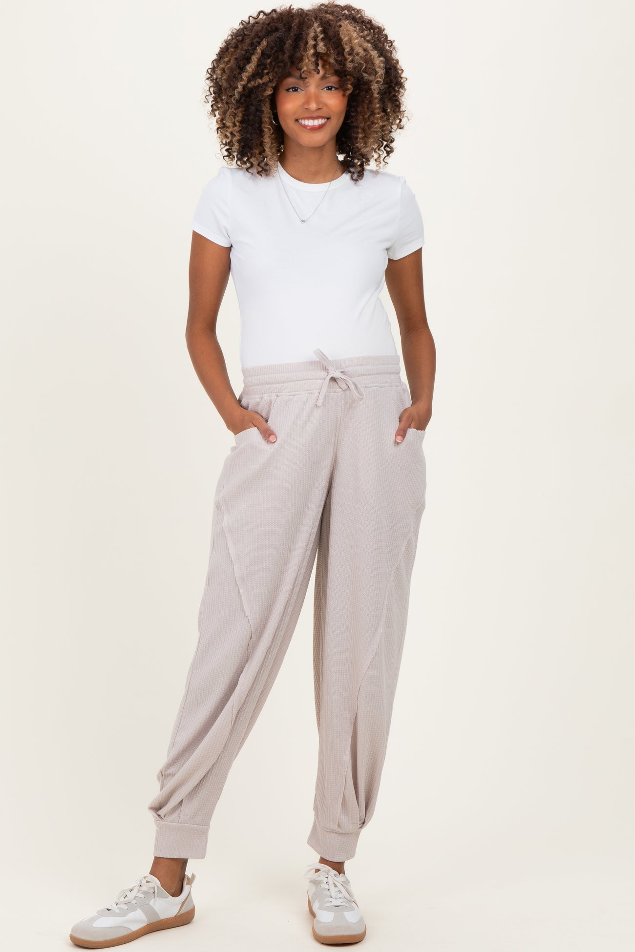 woman wearing a white short sleeve tee and beige maternity jogger pants with pockets, smiling and standing casually
