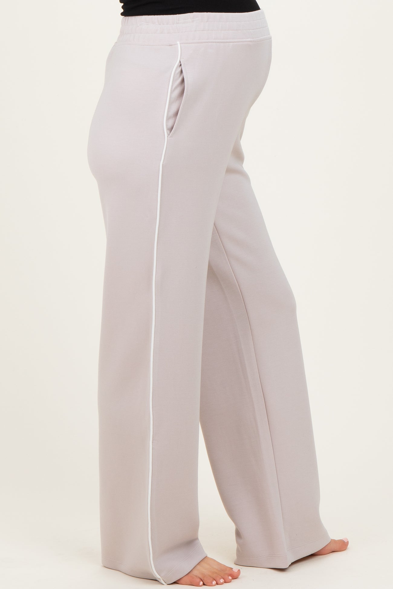 woman wearing light grey maternity pants with side pockets and white piping, showing her baby bump