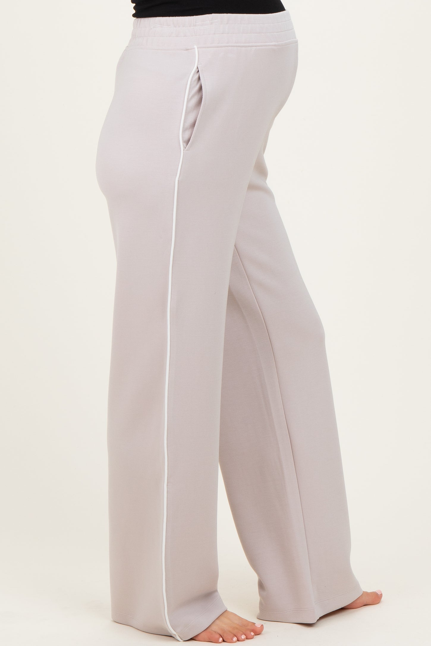 woman wearing light grey maternity pants with side pockets and white piping, showing her baby bump