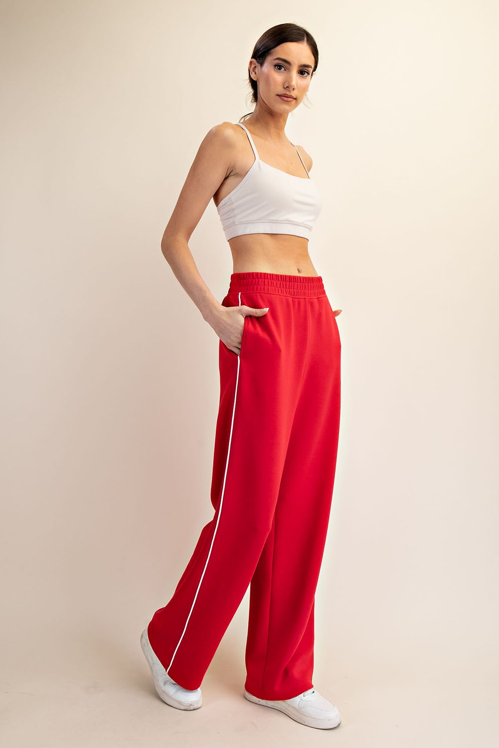 woman wearing a white crop top and red wide-leg sweatpants with side pockets and white piping details