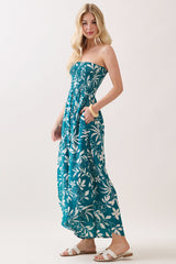 woman wearing a teal strapless maxi dress with white floral print and pockets, standing with one hand on her hip