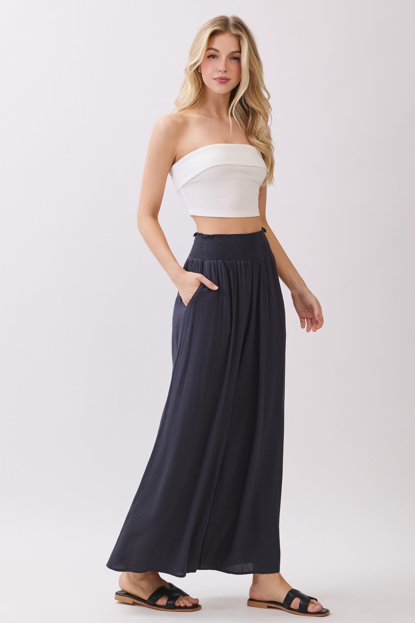 woman wearing a white strapless crop top and navy wide-leg pants with pockets, standing in a relaxed pose