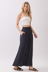 woman wearing a white strapless crop top and navy wide-leg pants with pockets, standing in a relaxed pose