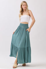 woman wearing a strapless white top and a teal maxi skirt with buttons and pockets, featuring a flowy design