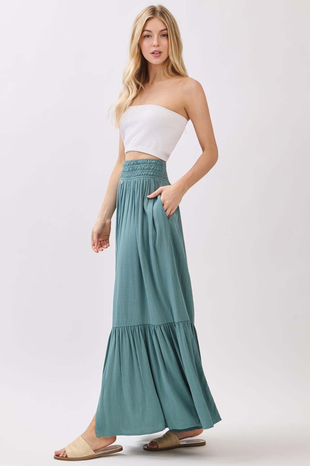 woman wearing a teal maxi skirt with a smocked waistband and pockets, paired with a white strapless top and sandals