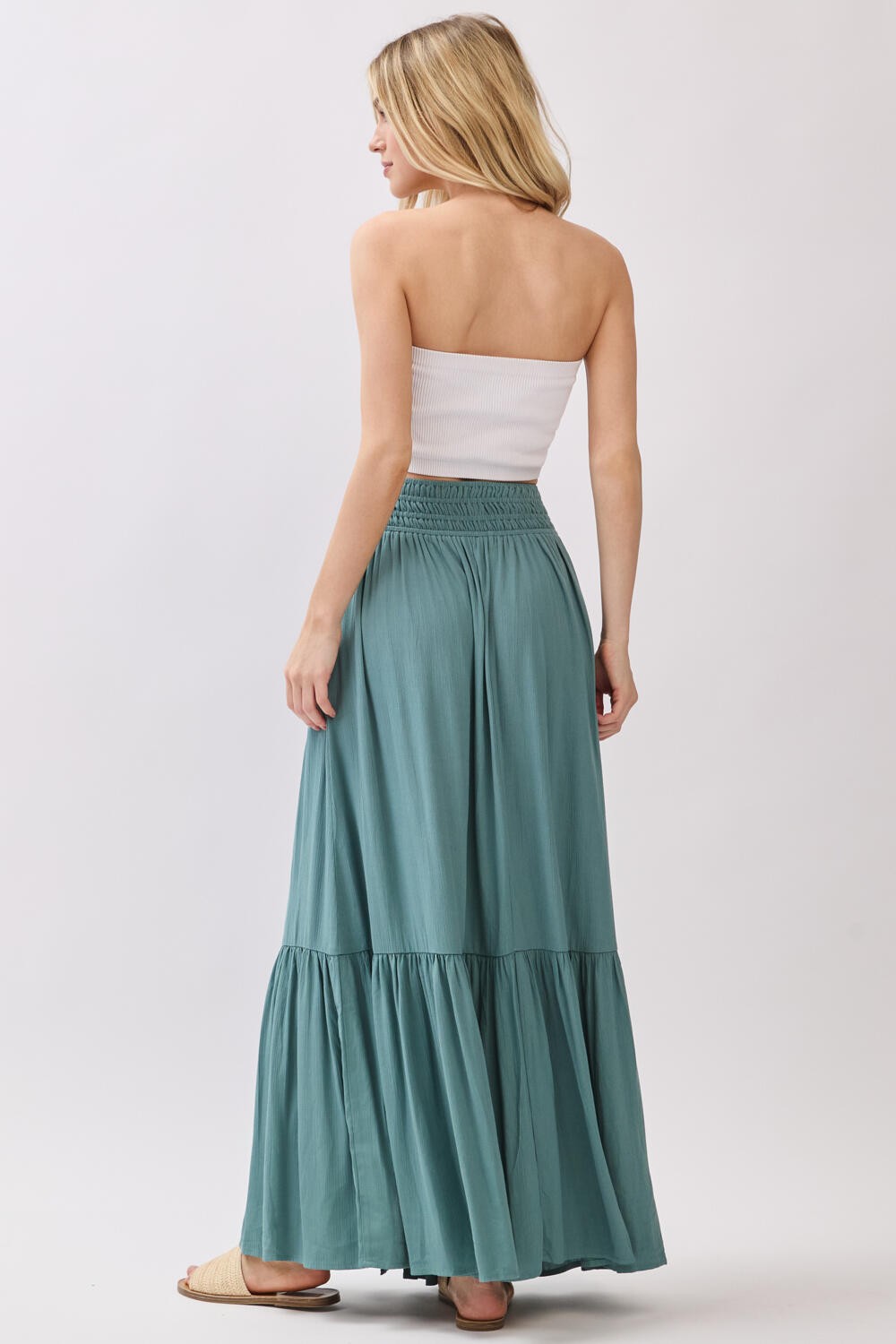 woman wearing a light green maxi skirt with a tiered design and a white strapless top, viewed from the back