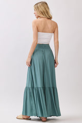 woman wearing a light green maxi skirt with a tiered design and a white strapless top, viewed from the back