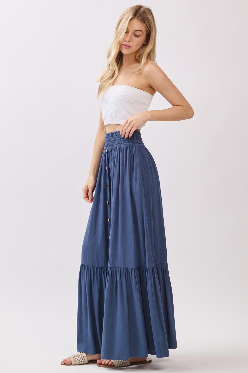 woman wearing a navy blue maxi skirt with a tiered design and button details, paired with a white strapless top