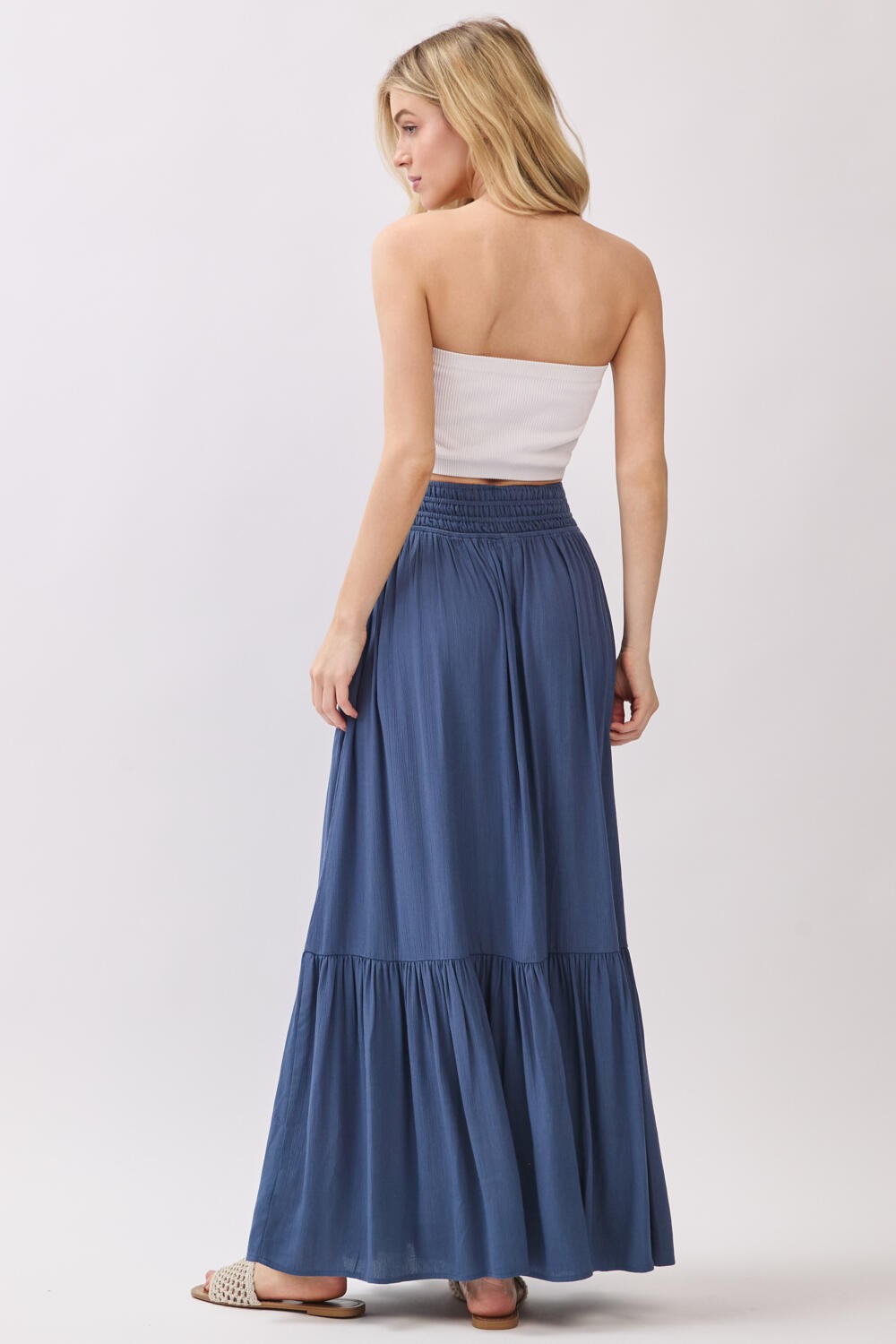 woman wearing a strapless white top and a long blue tiered maxi skirt, seen from the back