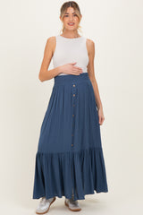 woman wearing a white sleeveless top and a long blue maternity skirt, holding her baby bump