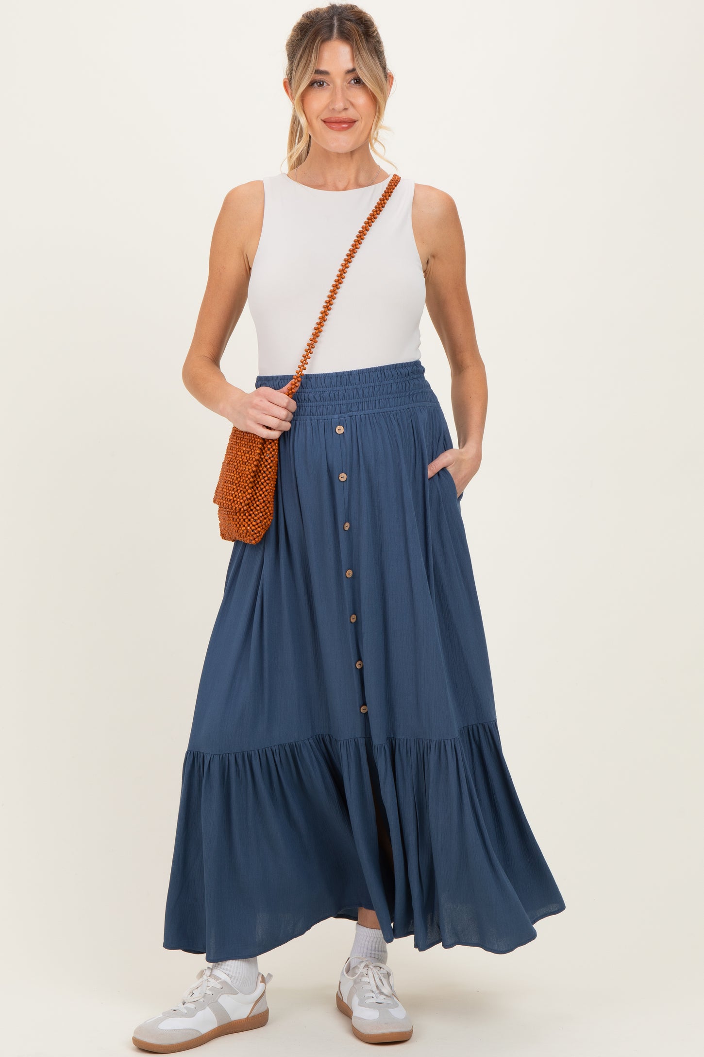 woman wearing a navy blue maternity maxi skirt with buttons and pockets, paired with a white tank top and holding a bag