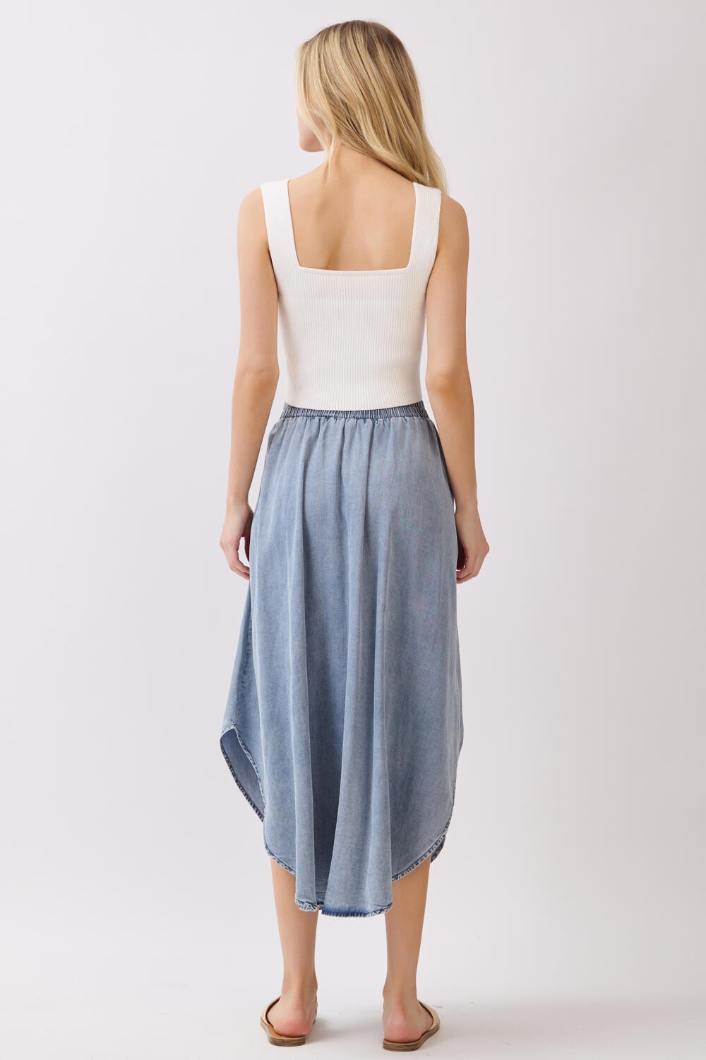 woman wearing a white ribbed tank top and a high-low denim skirt, viewed from the back
