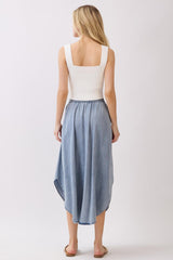 woman wearing a white ribbed tank top and a high-low denim skirt, viewed from the back